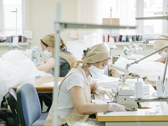 Women working at sewing machines in a textile factory wearing protective masks.