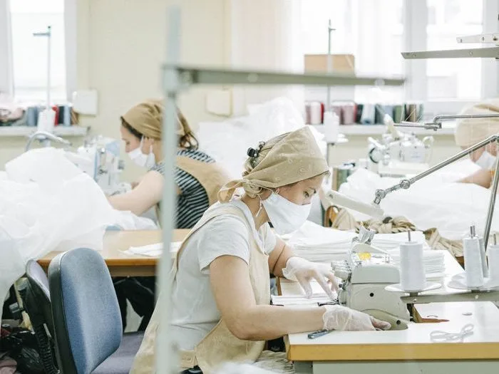 Women working at sewing machines in a textile factory wearing protective masks.